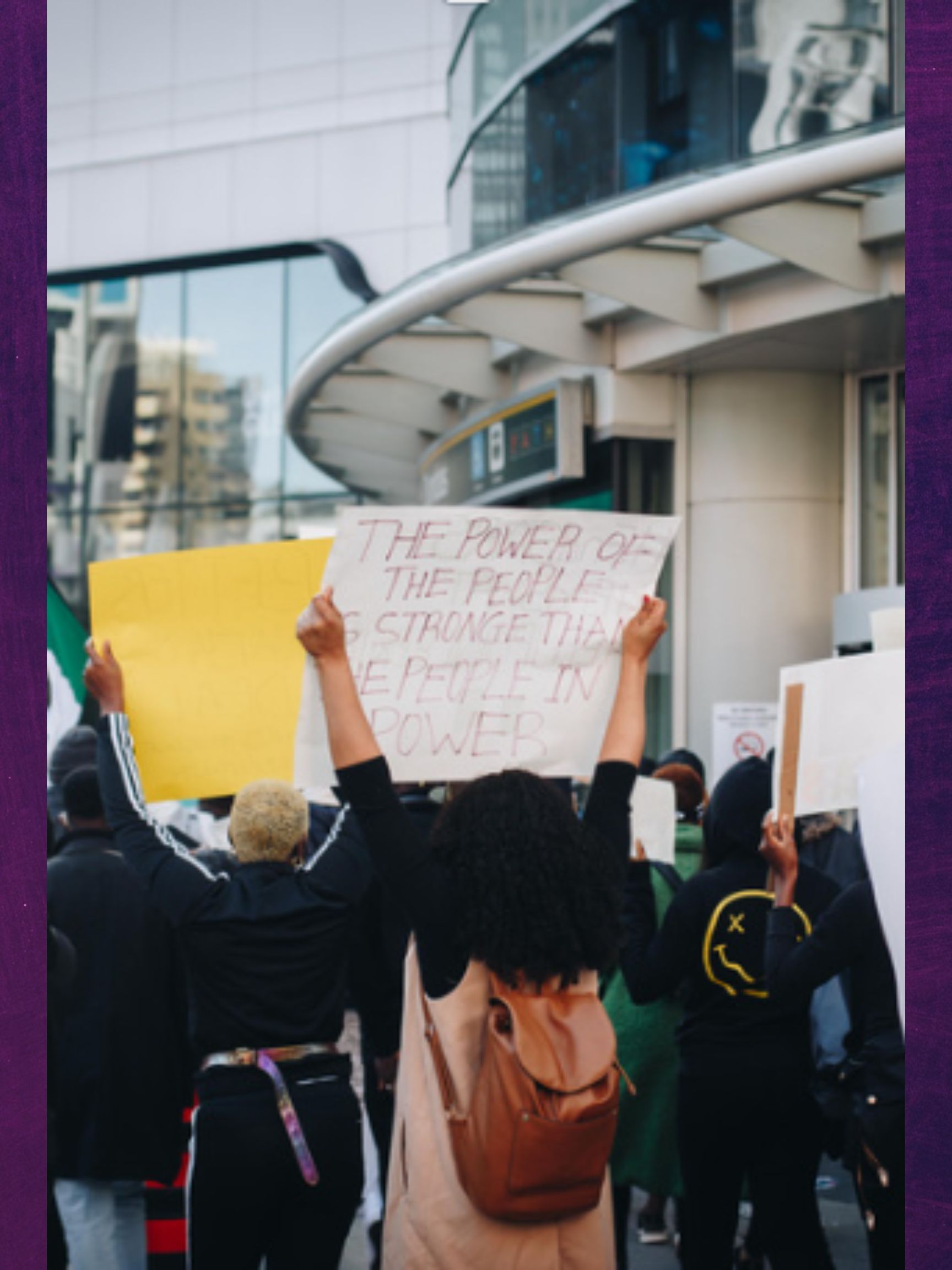 A group of people protesting. Main protest sign reads "The Power of the People is Stronger than the People in Power."